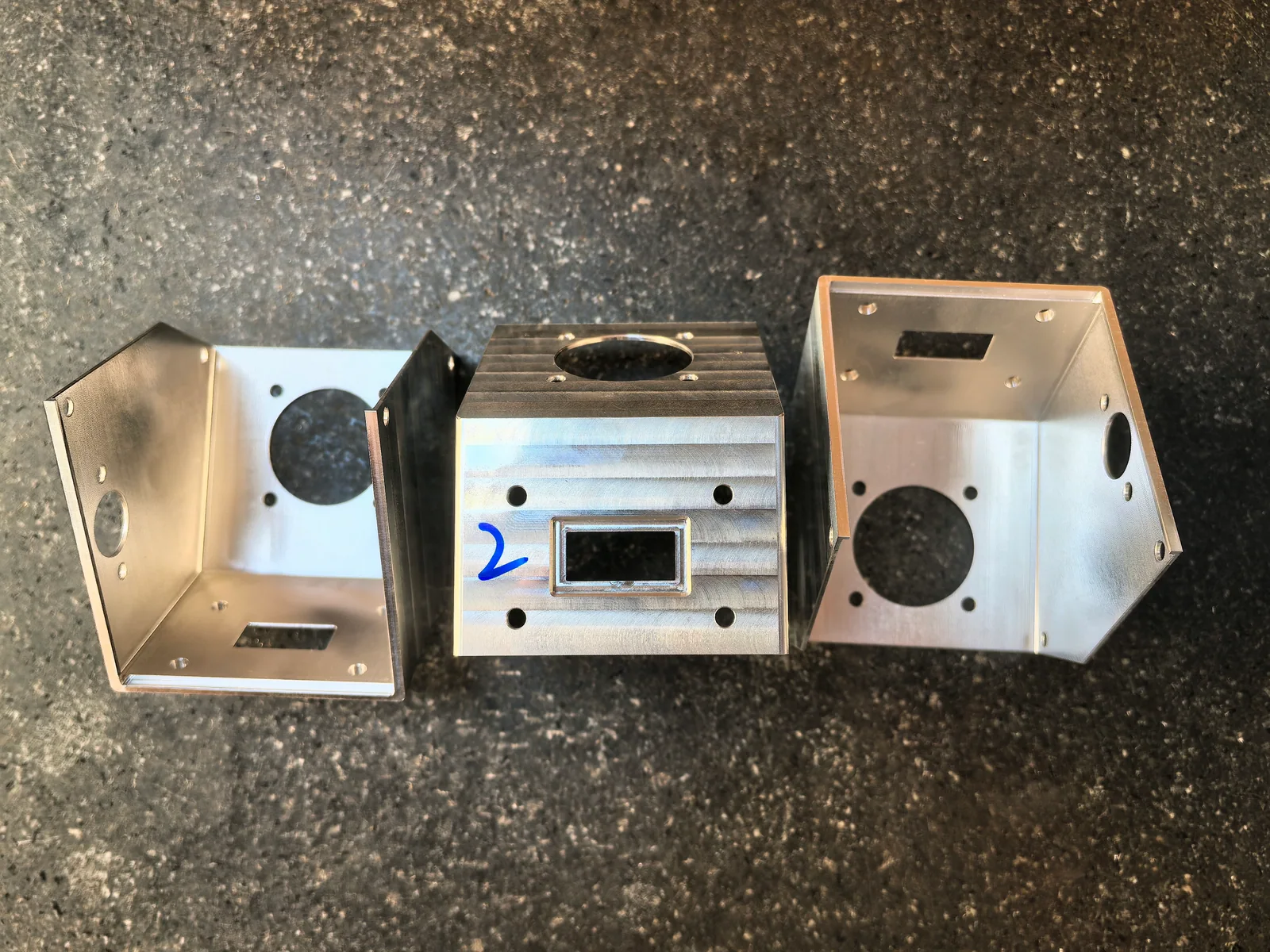 Three 2A12 aluminum cathode brackets in different orientations showing circular holes and rectangular openings